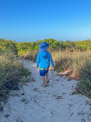 boy walking on sandy path weathing bathing suit and sun protection clothing