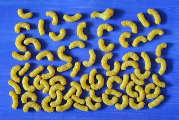 Gordijnen peanut curls, peanut puffs, peanut flavoured wotsits, delicious snacks, flat lay on blue background © Kirsten Hinte