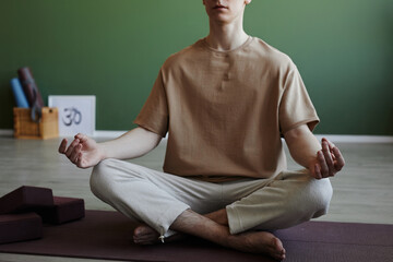 Minimal cropped shot of blissful young man meditating indoors sitting in lotus position, copy space