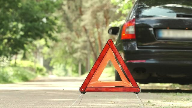 Red triangle, red emergency stop sign and black car with turned on blinkers. Emergency stop of the car with technical problems on the road. Safety procedure while having a vehicle broken down