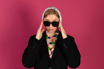 Portrait of a Beautiful tender young blonde hair girl is wearing a stylish black blazer and creative flowers attached to her chest and babushka head scarf. Isolated on pink background.