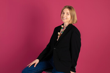 Portrait of a Beautiful tender young blonde hair girl is wearing a stylish black blazer and creative flowers attached to her chest or collar. isolated on pink background.