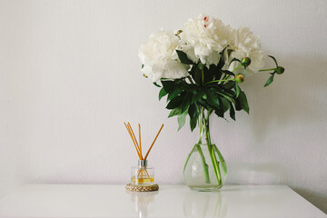 Still life details in home interior of living room. Incense sticks and vase with white peonies. Eco-friendly fragrance for the home. Cozy spring concept.