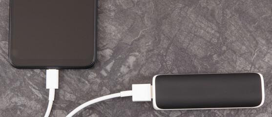Black smartphone with connected plug of external powerbank. Mobile phone charging. Place for text
