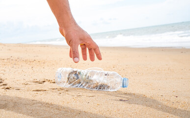 Hand picking up plastic bottle cleaning on the beach. Save the world concept. Environment, ecology...
