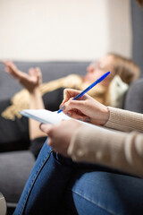 Female psychologist writes down main points from client stories in premise. Woman lying on grey...