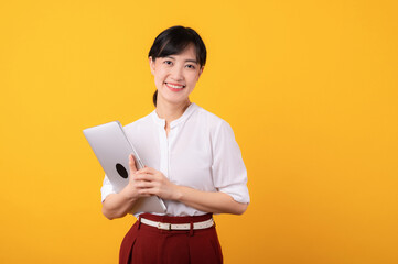 Portrait beautiful young asian woman enterpriser happy smile wearing white shirt and red plants showing confident body language gesture and holding laptop isolation on yellow background.