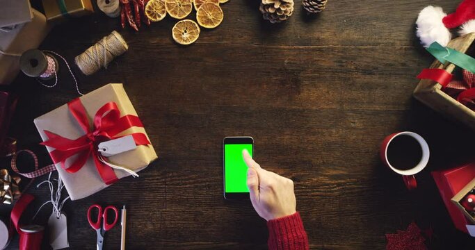 Christmas, gift and phone green screen in hands for package or box and mockup space. Above wooden table with person on smartphone for holiday wish list, creative ecommerce app or online shopping sale