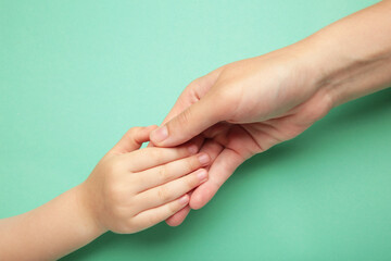 Mother holding daughter hand on mint background.