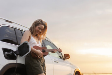 Portrait of young woman leaning on her car,playing on ukulele and enjoying summer time.