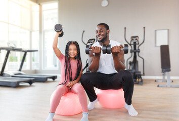Father teaches, trains daughter to lift dumbbells, cute, smiling, cheerful and happy.