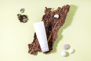 cream tube, tree bark and stones on a light green background