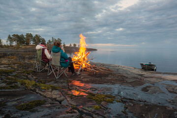 Girls sitting by the campfire on. the shore of the lake. Ladoga skerries, Karelia.