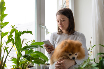 woman speak, send voice message on smartphone, sitting near green plants, flower with friend spitz...
