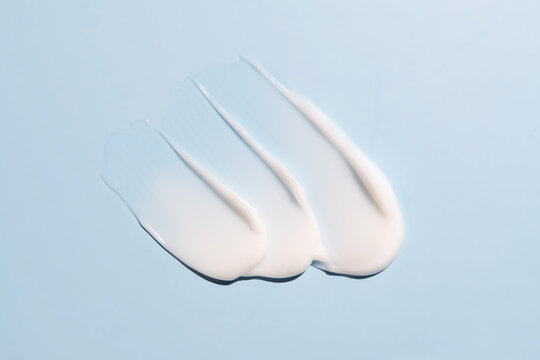 Texture of white cream on blue background. Smear of moisturizer close up. Lotion swatch. Beauty skin care product smear smudge. SPF sunscreen cream sample on blue background