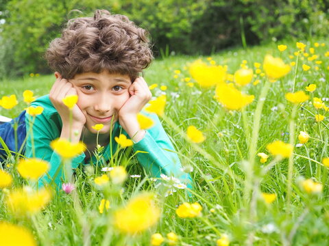 Cheerful little boy lying on the grass, camomile and celandine flowers, smiling. Happyness, childhood