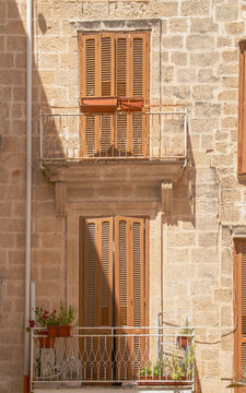 Casa al final de la calle Annunziata en el casco antiguo de Polignano a Mare, Italia. Fachada con dos antiguos balcones con contraventanas cerradas en una calle estrecha un d&iacute;a soleado.