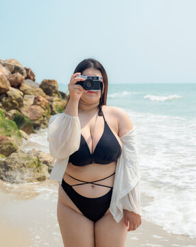 Portrait young woman asian chubby cute beautiful taking pictures with camera in bikini black sexy front viewpoint tropical sea beach white sand clean and bluesky calm Nature ocean Beautiful wave
