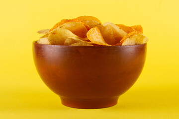 Potato chips in clay bowl isolated on yellow background. side view