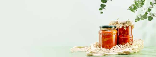 Probiotic food banner. Eco friendly still life with pickled or fermented vegetables in glass jars on textile bag on blue background with leaves and shadows. Home food preserving or canning. Copy space