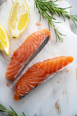 Raw salmon fillet steak with lemons and fresh herbs, over bright background.