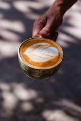 Hand holding coffee with milk in a ceramic cup against the background of the sun's rays. Delicious cappuccino with beautiful foam in the morning