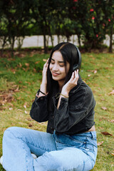 Portrait of a young woman listening to music on wireless headphones on a sunny afternoon in a park in South America.