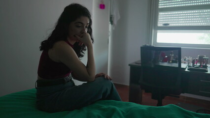 One pensive preoccupied young woman sits by bedside with contemplative expression. Female person in 30s struggling with inner emotions