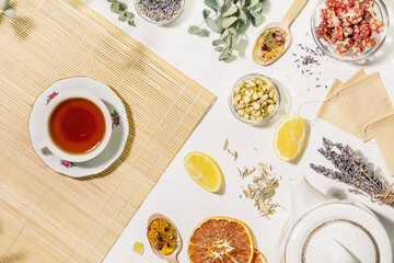 Natural healing tea from wild plants and flowers. Home herbal apothecary concept. Flat lay with dry flowers and herbs, lemon, paper tea bags, teapot and cup of tea on wooden napkin on white background