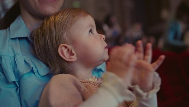 Happy baby girl having fun and clapping with admiration. Little child applauds looking at a performance in the theatre, a musical concert or a performance in a circus. Cultural event for children.