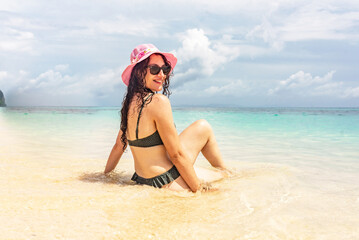 Girl sitting on the sand of a paradisiacal beach, enjoying a vacation day.