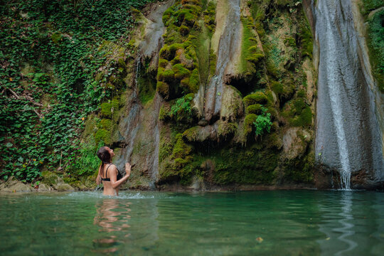 A girl swims in a mountain lake, in a spring. There are rocks, thickets, and jungles around