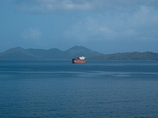Bulk carrier with red hull drifting in the sea near some land