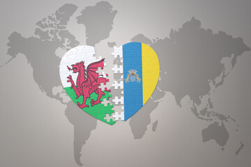 puzzle heart with the national flag of canary islands and wales on a world map background.Concept.