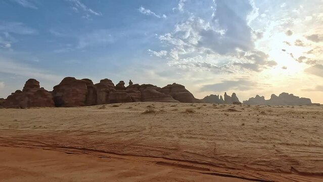 View from car driving at Hegra archaeological zone, flat desert with few small sandstone hills