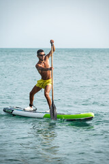 a sporty guy swims on a sup board with a paddle on the sea during the day against a beautiful sky