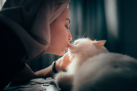 A girl with a towel on her head kisses a white cat on the nose