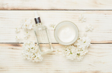 Composition with cosmetic bottles and flowers on wooden background, top view