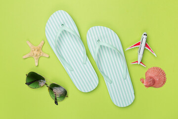 Flip flops with sunglasses and airplane on color background, top view