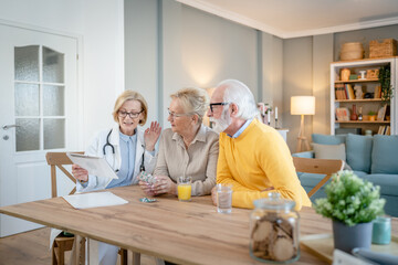 Home visit female doctor with senior man and woman couple at home talk