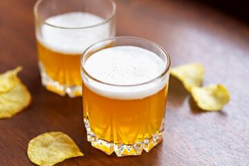 Glass of delicious fresh light unfiltered beer and potato chips on wooden background close up. Top view. Selective focus, defocus