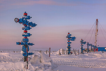 The Northern gas field. In the foreground is a row of gas producing wells. In the background, a mobile rig for well repair. A frosty winter day. The ground is covered with snow