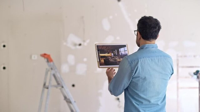 Man in glasses holding picture in hand looking at loft style interior design apartment owner standing against ladder near shabby wall in unfinished bedroom
