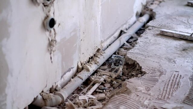 Shabby wall and drainage water pipe near hole in broken floor in bathroom renovation process in old apartment after past owners mess and disorder due to pipe installation