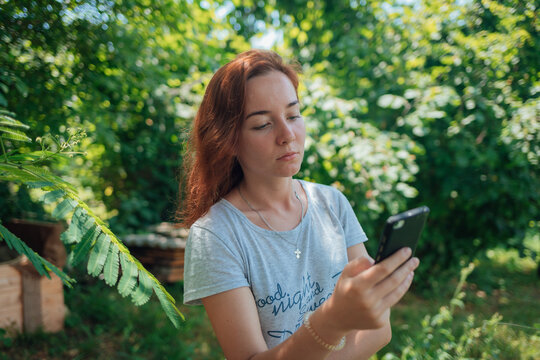 A girl uses  smartphone against a background of leaves