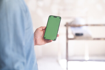 Hand of man holding mobile phone with green chromakey screen against construction safety equipment in unfinished room home owner looking for renovation ideas for living room in app