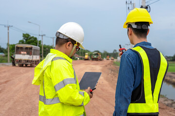 Asian engineer holding tablet and foreman using walkie talkie to control road construction, against...