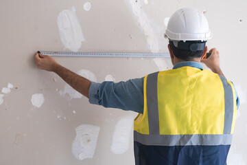 Professional architect in yellow vest puts tape-line to shabby wall to measure distance before...