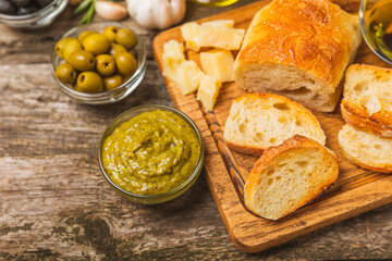 Italian ciabatta bread cut in slices with herbs, olives, pesto sauce, garlic and parmesan cheese on a wooden table. Fresh homemade Italian Ciabatta bread sliced with herbs and spices.Place for text. 