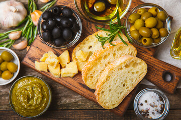 Italian ciabatta bread cut in slices with herbs, olives, pesto sauce, garlic and parmesan cheese on a wooden table. Fresh homemade Italian Ciabatta bread sliced with herbs and spices.Place for text. 
